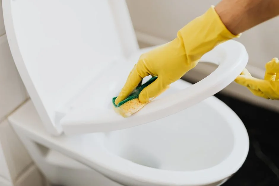 a-woman-in-a-green-shirt-and-black-gloves-vacuuming-a-gray-ottoman-5txz228u4eo